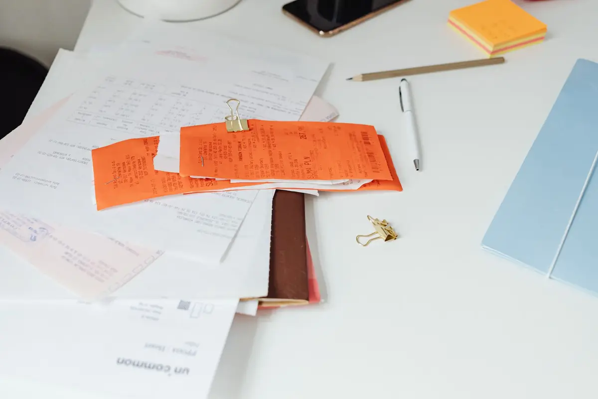 A desk with receipts, printed statements and a pen.